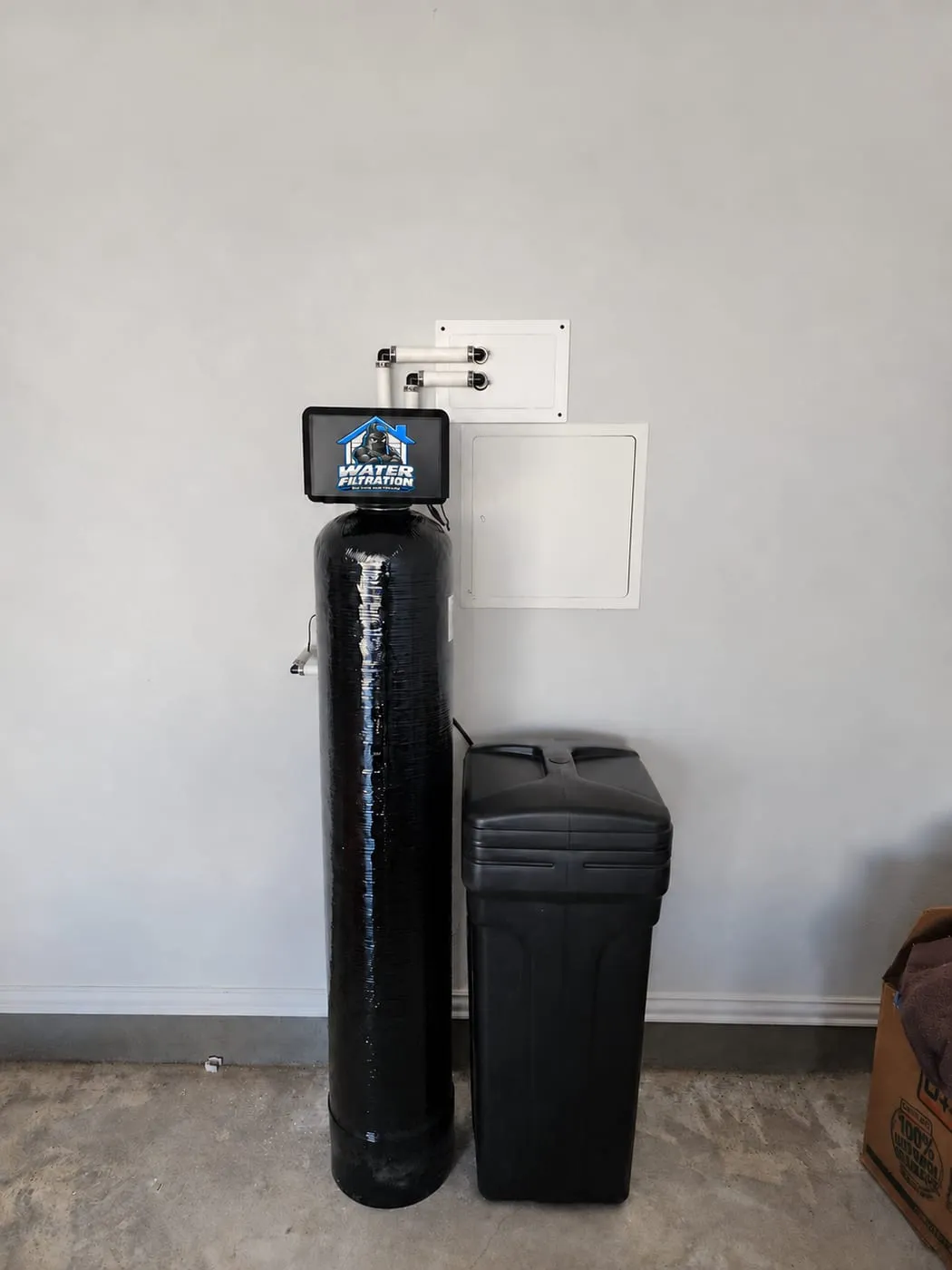 Softener and whole-house filter with the Water Filtration logo on the control valve, installed on a garage wall with access panels in Pike Creek, DE