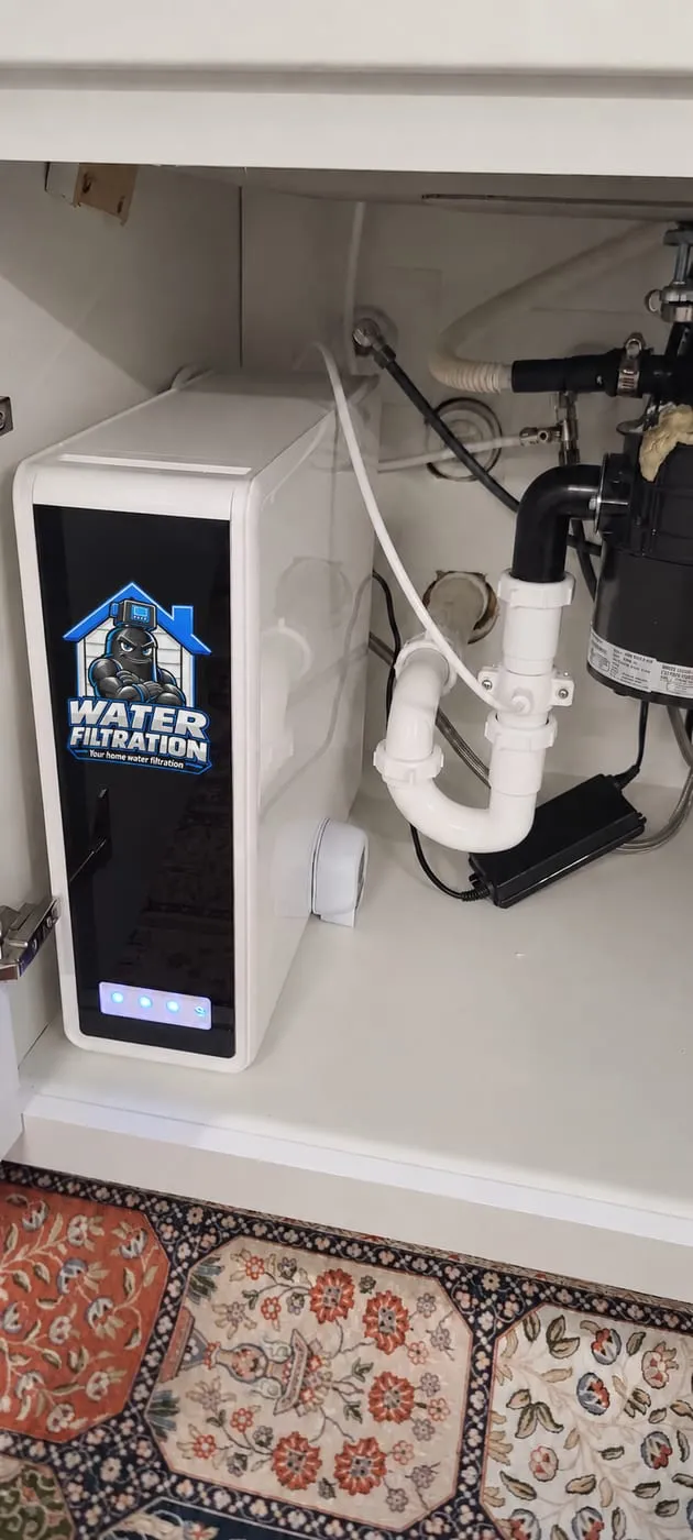 Under-sink reverse osmosis system with the Water Filtration logo beside a garbage disposal in a white kitchen cabinet in Middletown, DE