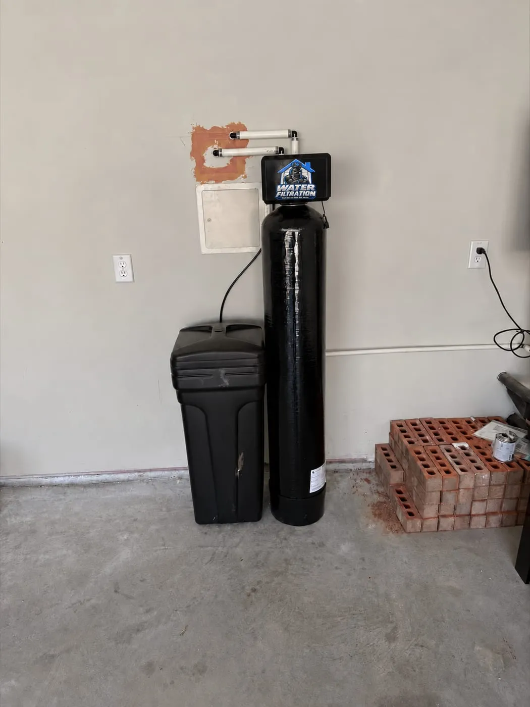 Water softener and filter tank with the Water Filtration logo valve installed on a garage wall with copper-free PVC plumbing in Smyrna, DE