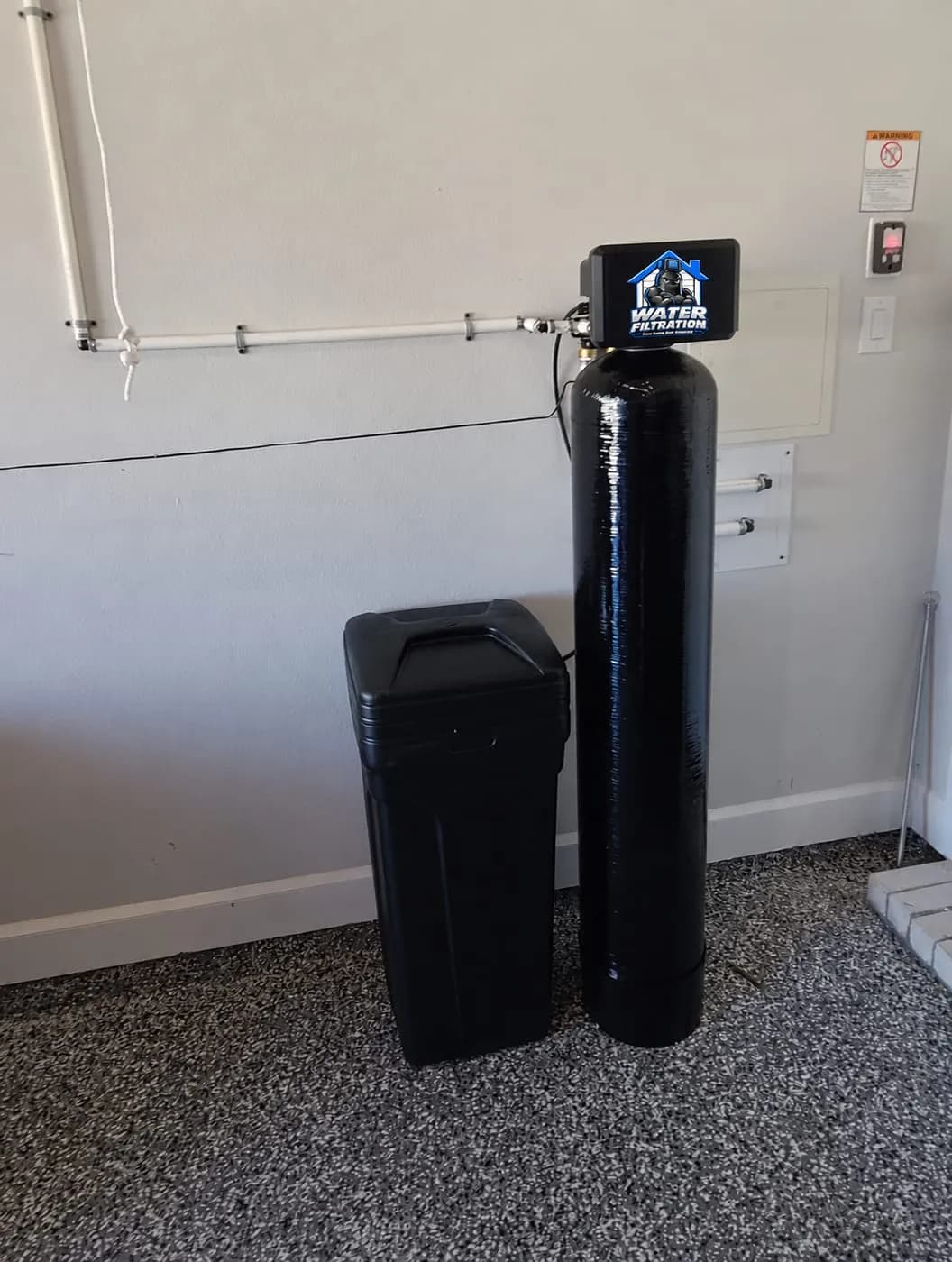 Water softener and filter tank with the Water Filtration logo valve cover installed in a garage with an epoxy floor in Claymont, DE